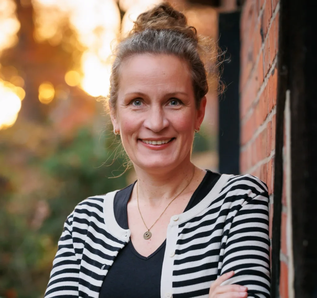 A portrait of expert Marthe Kniep. She is wearing a black-and-white striped cardigan and smiling in front of a brick wall. The photo accompanies her expert interview on hormone-free contraception and NFP with trackle.