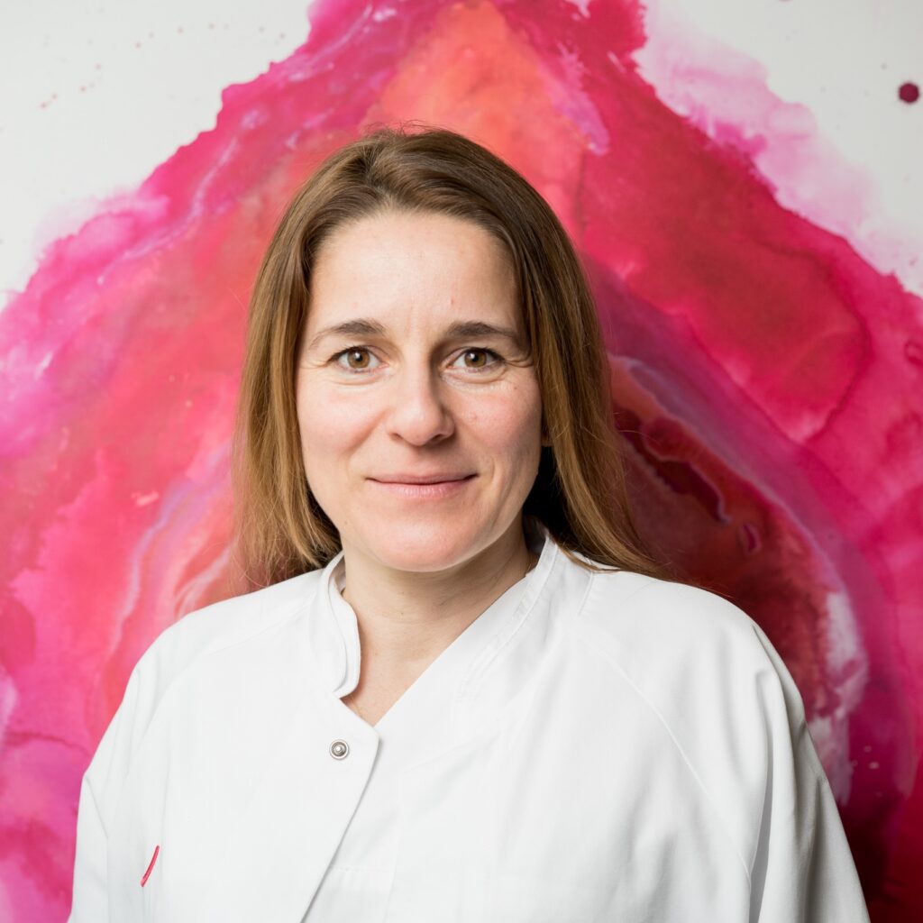 Portrait of Dr. Mandy Mangler, Chief of Gynecology and Obstetrics, wearing a white lab coat against a pink-and-red watercolor background.